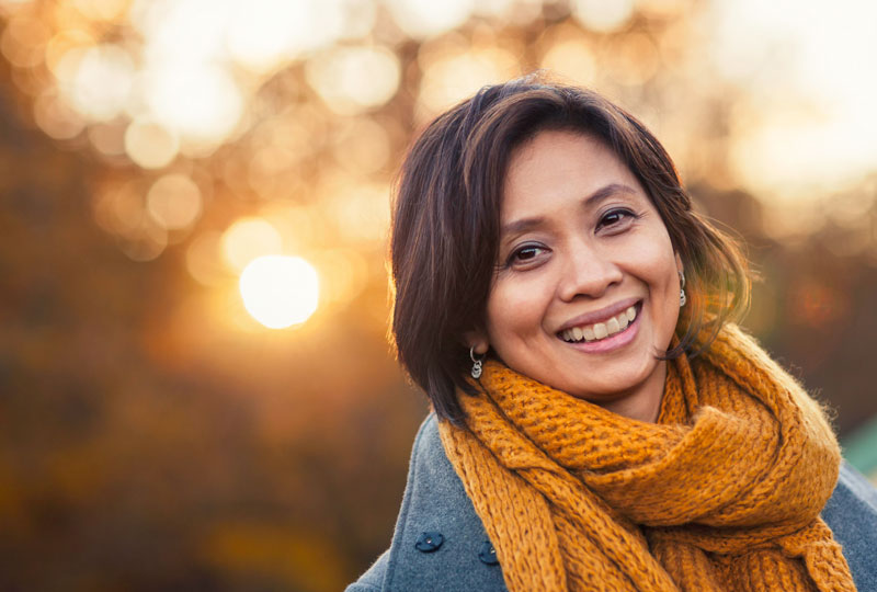 Asymmetrical head shot of a smiling Asian woman outdoors in late afternoon.