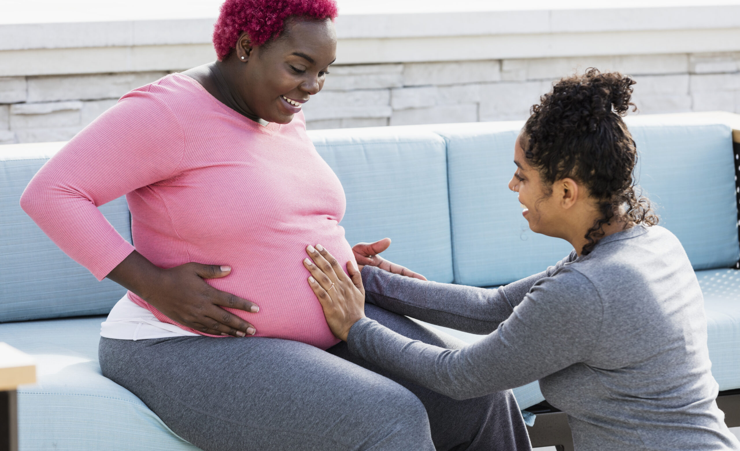 Doula kneeling, placing hands on pregnant patient's baby bump