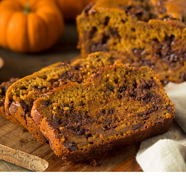 Closeup shot of slices of homemade pumpkin bread containing chocolate chips, on a cutting board.