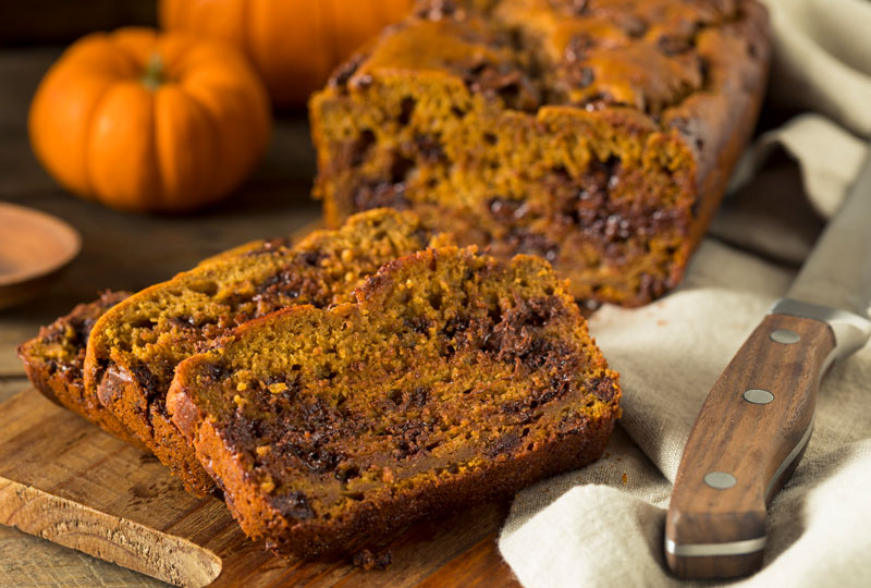 Closeup shot of slices of homemade pumpkin bread containing chocolate chips, on a cutting board.