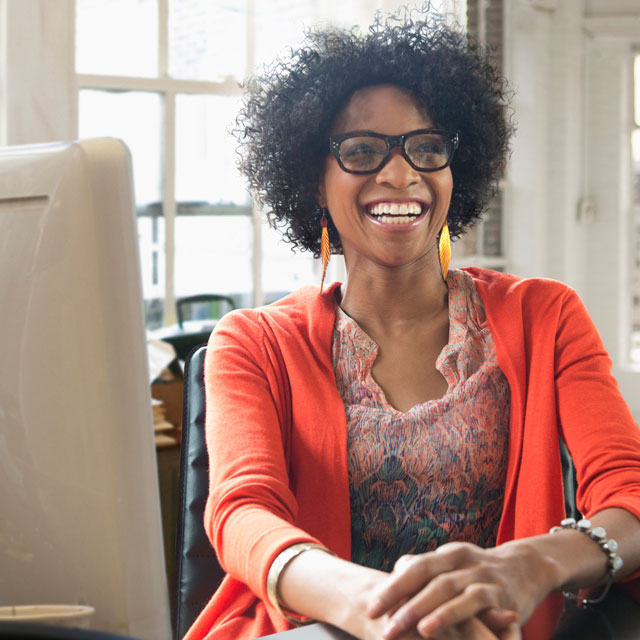 African-American woman smiling while sitting before a computer monitor.