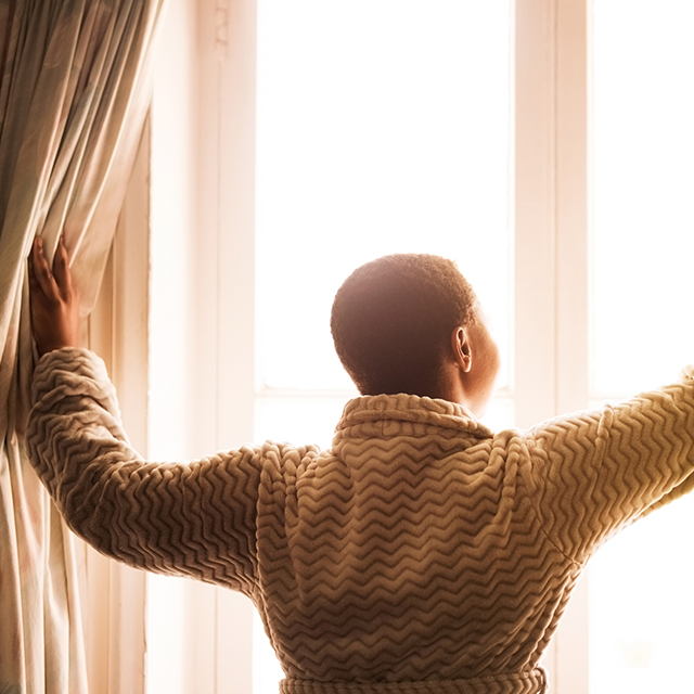 Woman opening curtains at dawn
